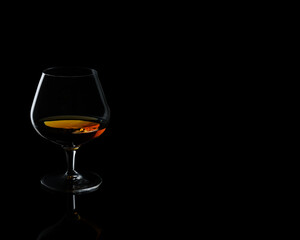 Snifter glass with cognac, brandy on a reflective surface. Extended dark background with copy space for placing logos and text. 