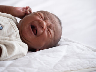 African American baby boy crying on a white bed.