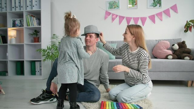 happy parenting, little cute girl puts hat on her dad head and kisses him during family time at home