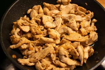Pieces of chicken fillet in a black skillet, small pieces of chicken meat cut into thin slices