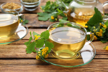 Glass cup of aromatic celandine tea and flowers on wooden table