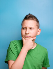 Studio shot of emotional adorable boy  covering face with hand being thoughtful, doubter and unsuspecting, showing true emotion. Portrait on blue background 