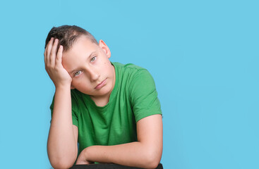 Studio shot of emotional adorable boy  covering head with hand being tired, headache,   showing true emotion. Portrait on blue background 