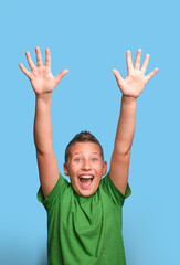 Studio shot of emotional adorable boy  smiling , showing happy emotion with hands up. Portrait on blue background 
