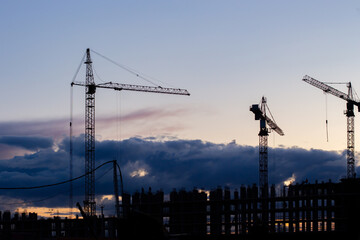 Three cranes and an unfinished residential skyscraper. Dramatic sky dusk landscape. Residential building construction