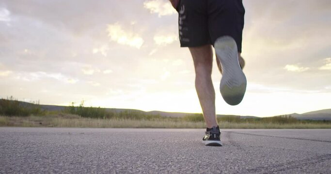 Rear view low angle slow motion of runner sprinting in distance during outdoors training for a marathon run in sunset time. 