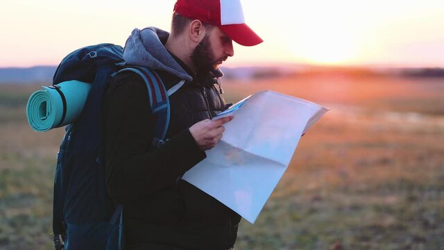 Adventure man with map and extreme explorer gear on mountain with sunset. Young man with backpack and map enjoying sunset, looking map. Tourist traveler on background landscape and sunlight in trip