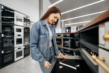 Fototapeta na wymiar Young brunette woman choosing new electric stove in a hypermarket