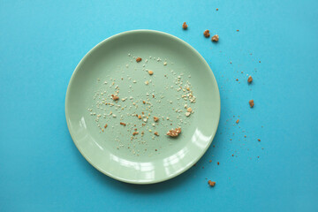 Emty white plate with some crumbs on light blue background. Finished party and holidays concept.