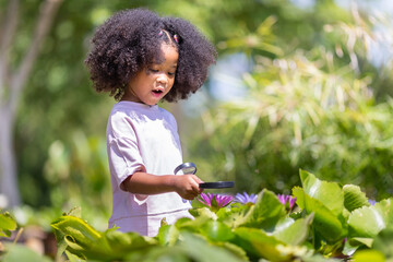 A curly-haired girl looks at a lotus flower with a magnifying glass.