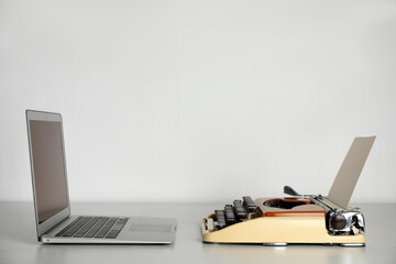 Old typewriter and laptop on table against light background, space for text. Concept of technology...