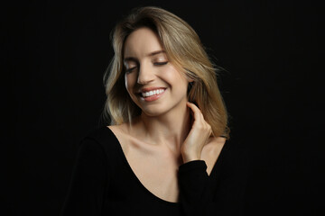 Portrait of happy young woman with beautiful blonde hair and charming smile on black background