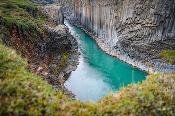 Man hiker in red jacket visit Studlagil basalt canyon, with rare volcanic basalt column formations,...