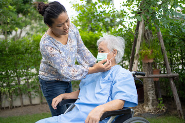 Help Asian senior or elderly old lady woman on wheelchair and wearing a face mask for protect safety infection Covid-19 Coronavirus in park.