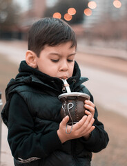 Argentine little boy drinking yerba mate in the park with bokeh in background