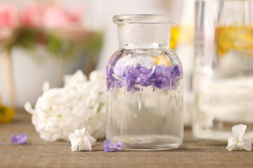 Fototapeta na wymiar Apothecary bottle with flowers on wooden table in laboratory, closeup. Extracting essential oil for perfumery and cosmetics