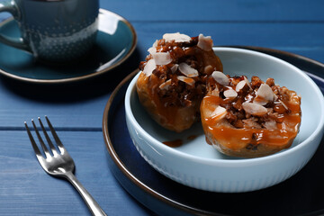 Delicious baked apple halves with nuts and caramel served on blue wooden table, space for text