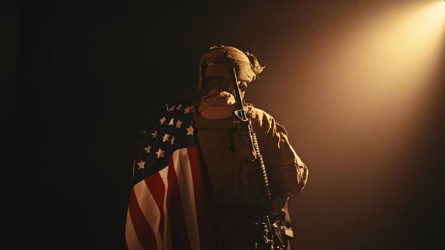 USMC soldier standing with his back to us in the dark holding USA national flag