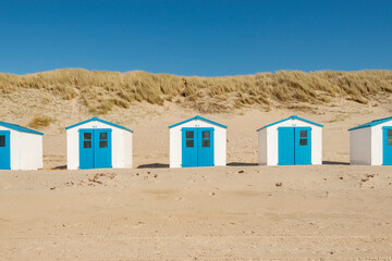 Blue and white beachhouses in the dunes at the beach on the island of Texel in the Netherlands. - obrazy, fototapety, plakaty