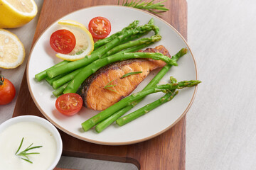 Delicious seasonal green asparagus and sliced smoked salmon on a rustic plate with lemon, salt, pepper, of lemon on a white plate . Baked salmon garnished with asparagus and tomatoes with herbs.
