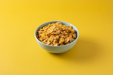 Corn flakes in a blue bowl on yellow background