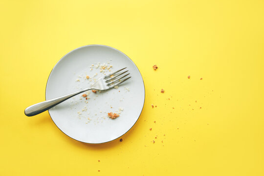 Conceptual image of the end of the holiday. Empty round plate with crumbs and fork on it on yellow background.