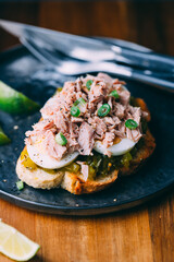Open sandwich with canned tuna, egg and pickled cucumber dressing served with lime.