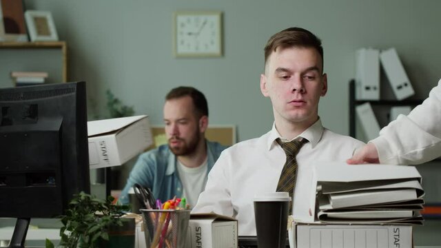 Tired irritated man with pile of folders working in office, employee having headache, exhausted worker with red eyes, pain in head, executive business people working. Bad mood, fatigue, lots of work. 