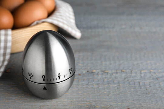 Kitchen timer and eggs on grey wooden table. Space for text