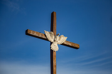 Uma cruz de madeira com imagem do Espírito Santo com o céu azul ao fundo.