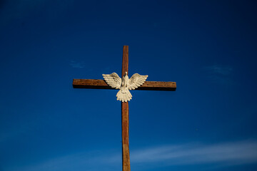 Uma cruz de madeira com imagem do Espírito Santo com o céu azul ao fundo.