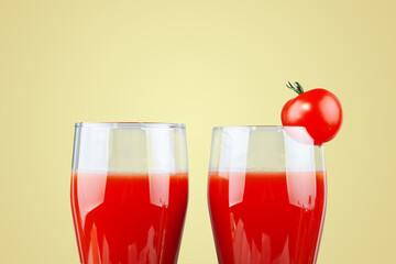 Two glasses with tomato juice and a small tomato on a yellow background.