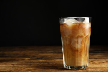 Glass of coffee with milk and ice cubes on wooden table. Space for text