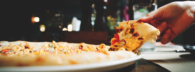 woman Hand takes a slice of meat Pizza with Mozzarella cheese, salami, Tomatoes, pepper, ham in cafe