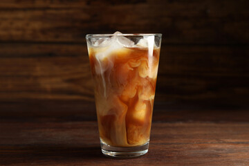 Glass of coffee with milk and ice cubes on wooden table