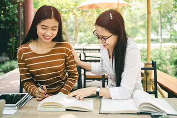 Asian woman sitting pointing studying examining, Tutor books with friends Young students campus helps friend catching up and learning. People learning education