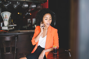 Fototapeta na wymiar Positive young black woman talking on smartphone in cafe