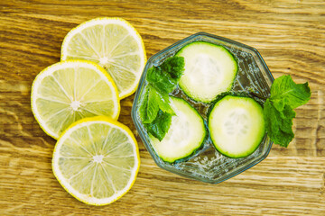 Cucumber and mint lemonade in a glass cup. Lemon slices on a light wooden background