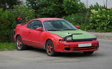 Fototapeta na wymiar An old broken down red sports car with a green hood, Iskrovsky Prospekt, Saint Petersburg, Russia, June 2021