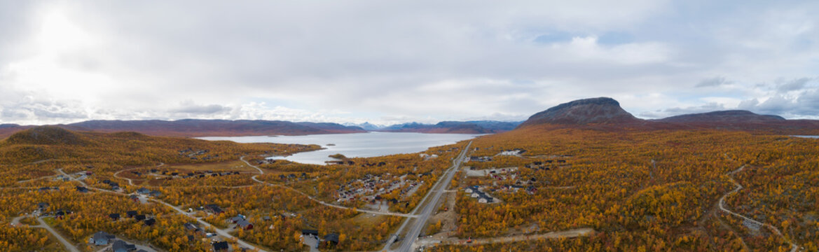 Aerial view of the road and village Kilpisjarvi in mountain valley at autumn. Saana mountain. Trees with red, yellow and orange leaves. Lapland.