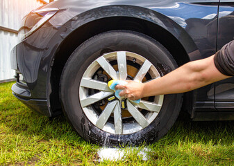 Hand washing car rims with a sponge with car shampoo for cleaning dirt and giving shine, close-up