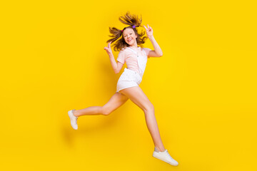 Fototapeta na wymiar Full length body size view of attractive trendy cheerful girl jumping running showing v-sign isolated over bright yellow color background