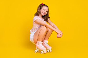 Portrait of attractive cheerful girl sitting wearing riding skates weekend rest isolated over bright yellow color background