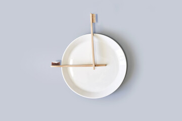 Ecology toothbrush on grey background. Brush on plate. Breakfast concept. Sustainable mouth product. Zero waste lifestyle. Organic accessory. Dental health at home. Biodegradable recycle. Clock