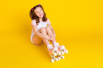 Full length photo of schoolgirl wearing rollers sit floor look empty space isolated bright yellow...