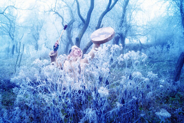 beautiful shamanic girl playing on shaman frame drum in the nature.
