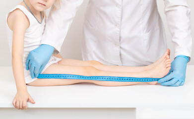 A doctor in blue gloves with a measuring tape measures the length of the legs of a 4-year-old caucasian girl. Child development and growth concept - obrazy, fototapety, plakaty