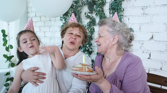 Three woman generation celebrate senior woman 85th birthday, grandma holds cake and happy blowing out candle all together. Female family enjoy, respect and warm relation. Celebration concept