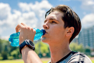 Athletic young man drinking water after running on the running track.