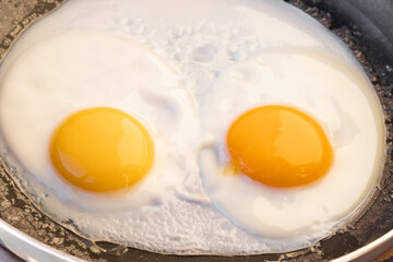 Cooked fried eggs with two bright round raw yolks in a black skillet. Simple breakfast option. Top view, close-up. Look like eyes